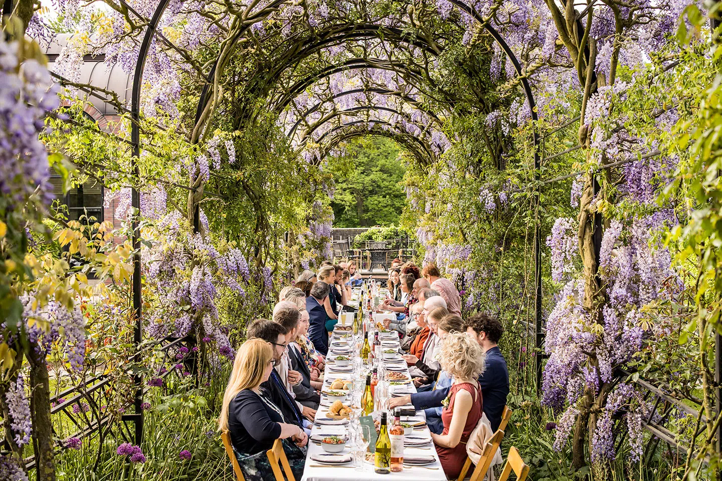 Gasten aan lange tafels tijdens een bruiloft in de tuin van Tuin de Lage Oorsprong