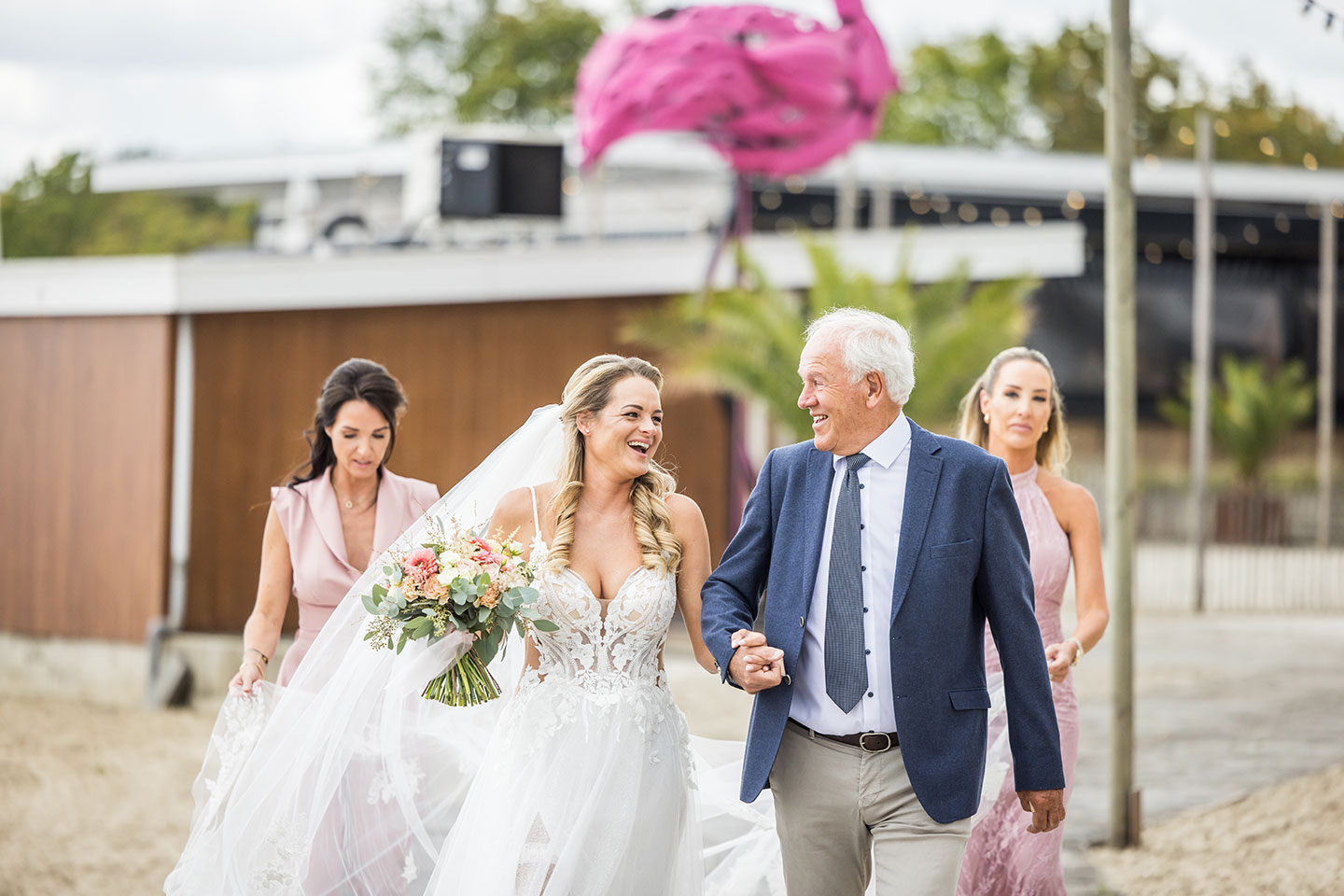 Bruid loopt met vader naar ceremonie van een bruiloft bij Beachclub Sunrise